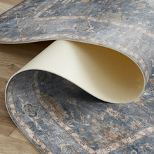 Load image into Gallery viewer, Rolling up a blue patterned rug on a wooden floor