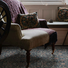 Load image into Gallery viewer, A vintage-style upholstered armchair in a cozy room setting, featuring a beige fabric seat, dark wood legs, a patterned throw blanket, and a matching decorative throw pillow. The chair is positioned next to a window with a built-in bench and a matching patterned cushion.