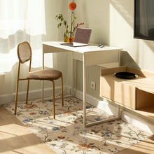 Load image into Gallery viewer, A modern home office corner featuring a white desk with a metal frame, a woven-back chair with a brown cushion, and a floral area rug. A laptop, vase of flowers, and a small side cabinet are arranged on the floor in warm natural light.