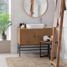 Load image into Gallery viewer, Bathroom with wooden vanity, round mirror, a plant and a beighe area mat