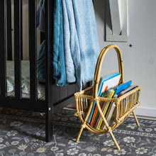 Load image into Gallery viewer, Wicker magazine rack with books next to a black cabinet with a blue towel on a patterned rug.