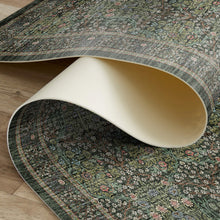 Load image into Gallery viewer, A rolled section of a traditional patterned area rug with a dark green base and floral motifs, shown on a light wood floor.
