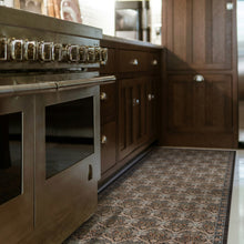 Load image into Gallery viewer, A close-up view of a patterned area rug in a modern kitchen, positioned between a stainless steel range and dark wood cabinetry.