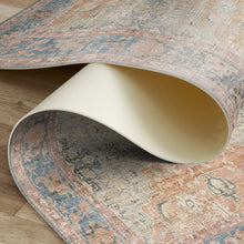 Load image into Gallery viewer, Close-up of a patterned rug with a rolled-up section on a wooden floor.