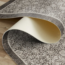 Load image into Gallery viewer, A close-up of a patterned area rug partially rolled up, showing both the top decorative side and the cream-colored underside, placed on a light wood floor.