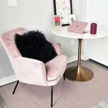 Load image into Gallery viewer, A pink velvet armchair with a fluffy black throw pillow, positioned next to a white round table with a gold pedestal base in a bright room.