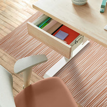 Load image into Gallery viewer, A light wood desk with an open drawer showing office supplies, paired with a peach-colored office chair on a striped chair mat over a wooden floor.