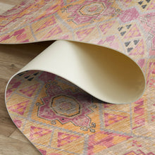 Load image into Gallery viewer, Close-up of a patterned rug being rolled out on a wooden floor.
