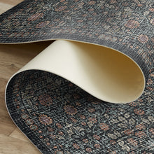 Load image into Gallery viewer, A close-up of a rolled area rug showing its dark charcoal gray patterned top and cream underside, laid on a light wood floor.
