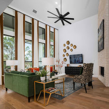 Load image into Gallery viewer, A modern living room interior with a green velvet sofa, a zebra-print accent chair, a gold-framed coffee table, tall windows with brown and cream drapes, and a black ceiling fan.

