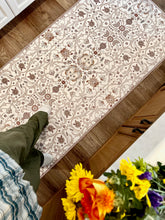 Load image into Gallery viewer, Patterned rug on a wooden floor with a person walking on it, surrounded by flowers.
