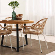 Dining table with wicker chairs and a plant in a room with white curtains and a large area rug