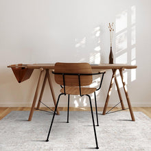 Load image into Gallery viewer, Wooden desk with a chair in a bright room with sunlight streaming through a window.
