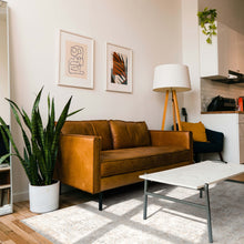 Load image into Gallery viewer, Modern living room with brown leather sofa, white coffee table, and decorative plants.
