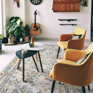 Living room with yellow armchairs, a guitar, and decorative items on a floral rug.