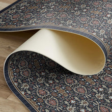 Load image into Gallery viewer, A rolled section of a traditional oriental area rug with a dark navy blue base and intricate floral motifs in beige, rust red, and gold, shown on a light wood floor.

