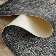 Load image into Gallery viewer, A close-up of a rolled area rug showing its distressed traditional pattern in muted teal, gray, and tan, with a cream underside, laid over a light wood floor.

