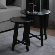 Two black side tables with cylindrical objects on a light-colored rug.