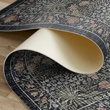 Load image into Gallery viewer, A close-up of a patterned area vinyl rug partially rolled over to show both the top and bottom sides. The top side features an intricate floral and geometric design in black, beige, and muted pink tones, while the underside is a solid cream color.
