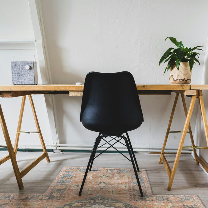 Black chair in front of a wooden desk with a plant on a white wall placed on a desk mat