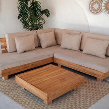 Load image into Gallery viewer, Beige sectional sofa with wooden coffee table in a room with a plant and decorative wall items and brown vinyl rug.
