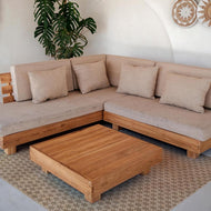 Beige sectional sofa with wooden coffee table in a room with a plant and decorative wall items and brown vinyl rug.