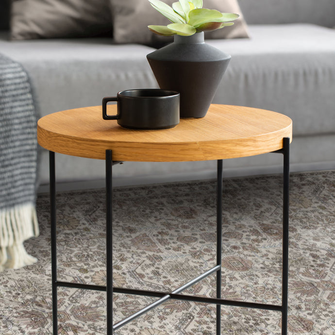 Small round wooden table with black metal legs, featuring a black mug and vase on a living room floor.