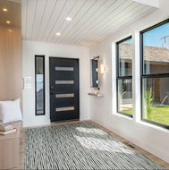 Modern interior of a home with a black door, striped rug, and large windows.