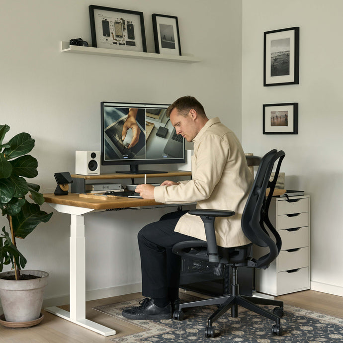 Man sitting at a desk with a computer setup in a home office over a decorative chair mat.