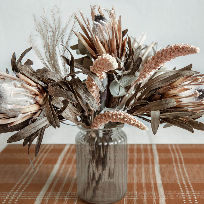 Dried floral arrangement in a glass vase on a table with a plaid tablecloth.