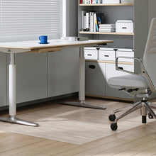 Load image into Gallery viewer, A modern adjustable height standing desk with a light wood top and white legs, shown in a bright home office setting next to a white office chair.
