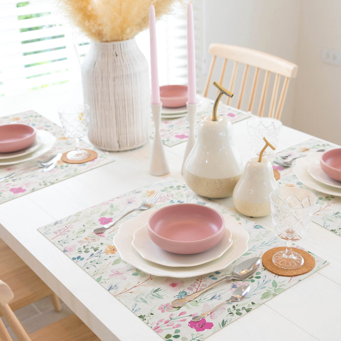 Dining table setting with floral placemats, pink bowls, and decorative vases.