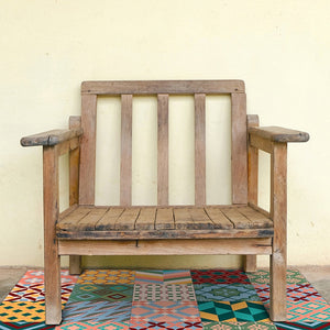 Orange and colorful patchwork  vinyl mat with Spanish tile design below a rustic wooden bench
