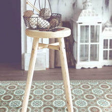 Load image into Gallery viewer, Brown and green vintage vinyl floor mat with Spanish tile designs under a stool chair
